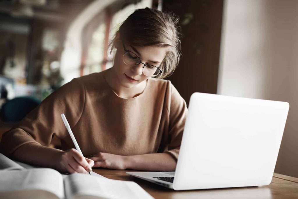 hardworking-focused-woman-trendy-glasses-concentrating-writing-essay-sitting-cozy-cafe-near-laptop-working-making-notes-carefully-4